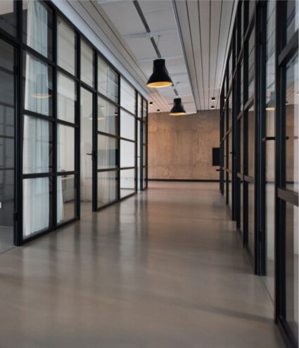 A hallway of a modern office building with black paned floor to ceiling windows on either side.